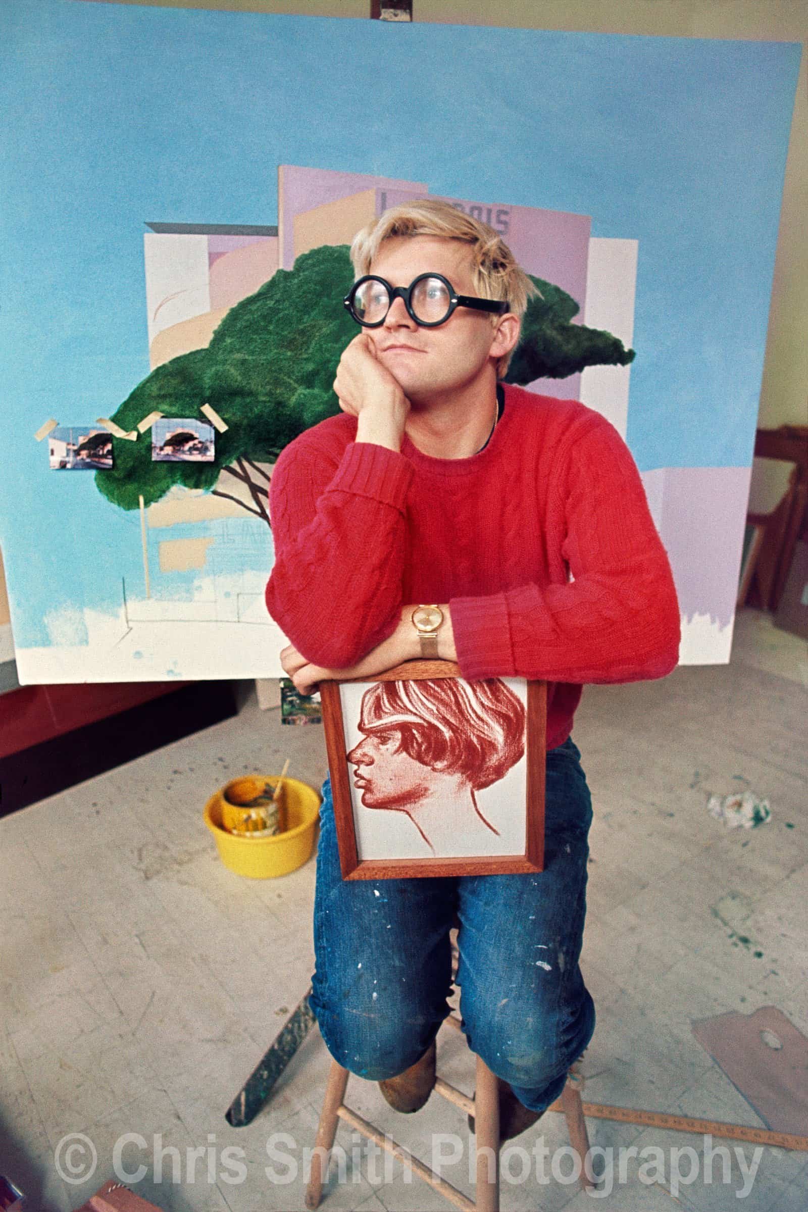 David Hockney sitting on stool with painting in Kensington studio 1968 photograph by Chris Smith